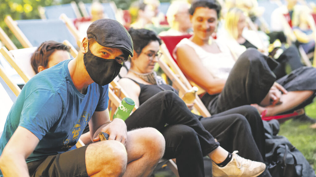ein junger Mann mit Mundschutz und seine zwei Freunde genießen im Liegestuhl das Filmfestival