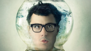ein Junger Mann mit einer schwarzen Brill steckt mit dem Kopf in einer durchsichtigen Glaskugel