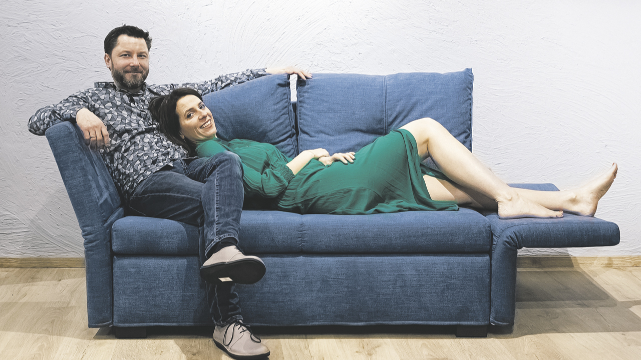 eine junges Paar liegt bzw. sitzt gemütlich auf einem blauen Sofa