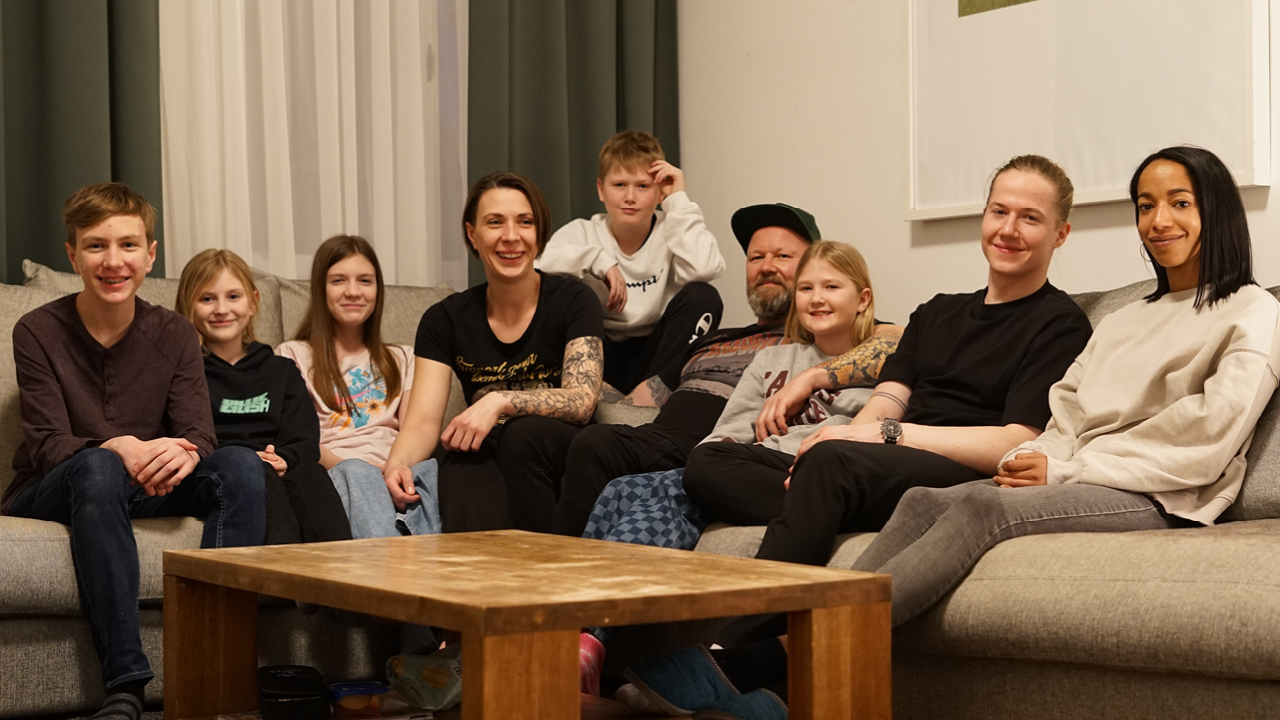 eine große Familie: die Eltern sitzen mit ihren sieben Kindern auf einem Sofa, davor ein kleiner Holztisch