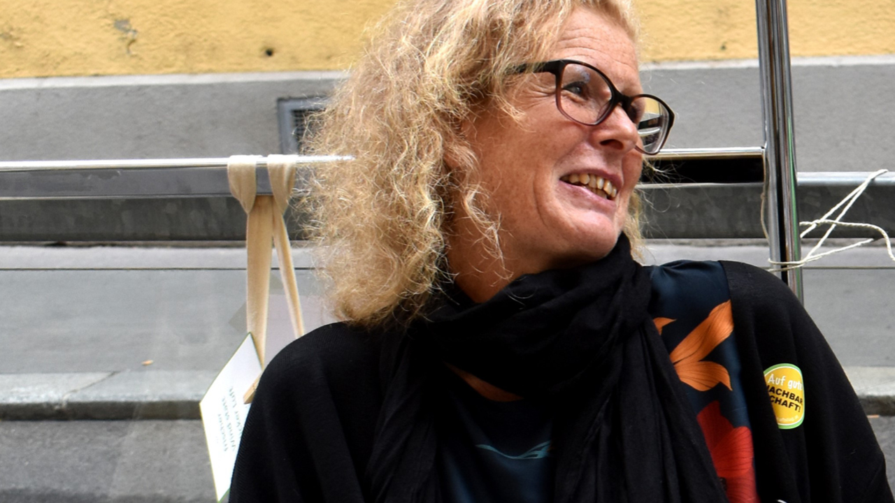 Portrait einer Frau mit schwarzer Brille und blonden Locken; lacht mit Kopf zur Seite gedreht