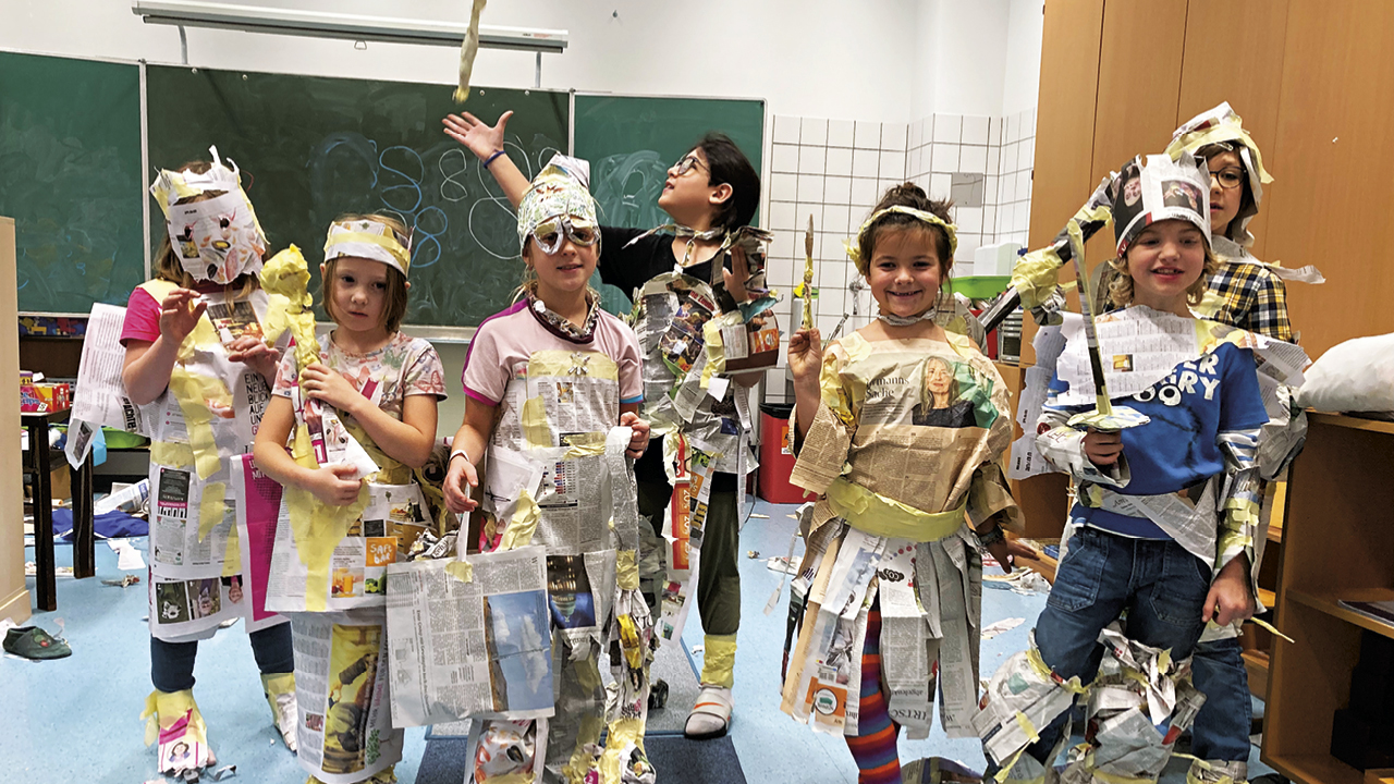 Eine Gruppe Kinder vor einer Schultafel in Verkleidung aus Zeitungspapier