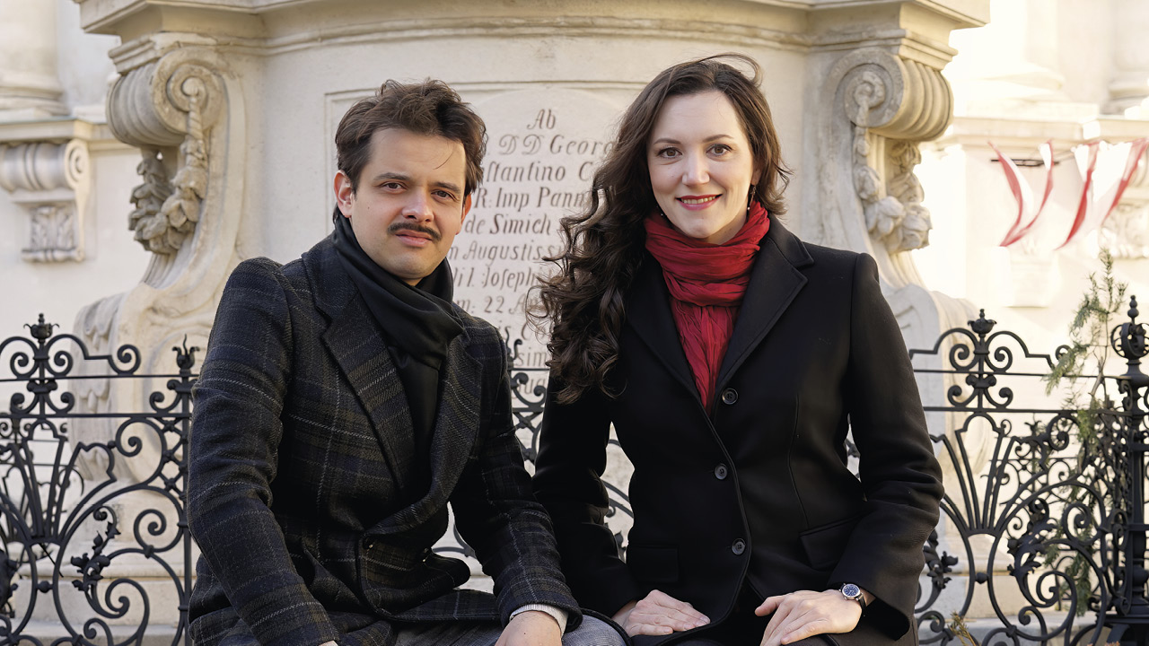 Künstlerpaar sitzt im Freien vor einer historischen Säule